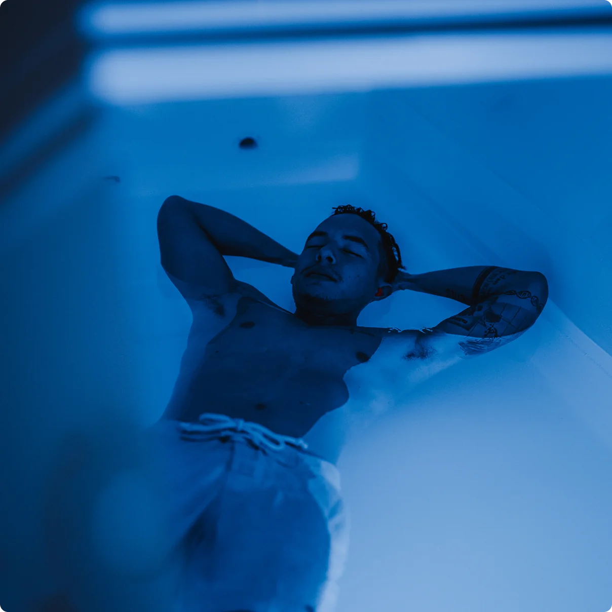 Man lying in a flotation therapy tank, relaxed during a float session with ambient lighting