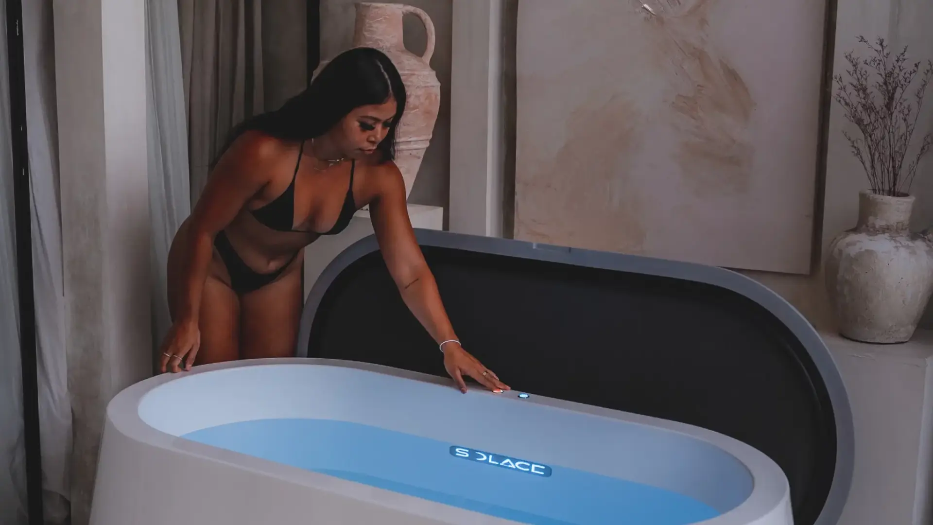Woman activating the internal lighting on a Solace ice bath at night, residential interior