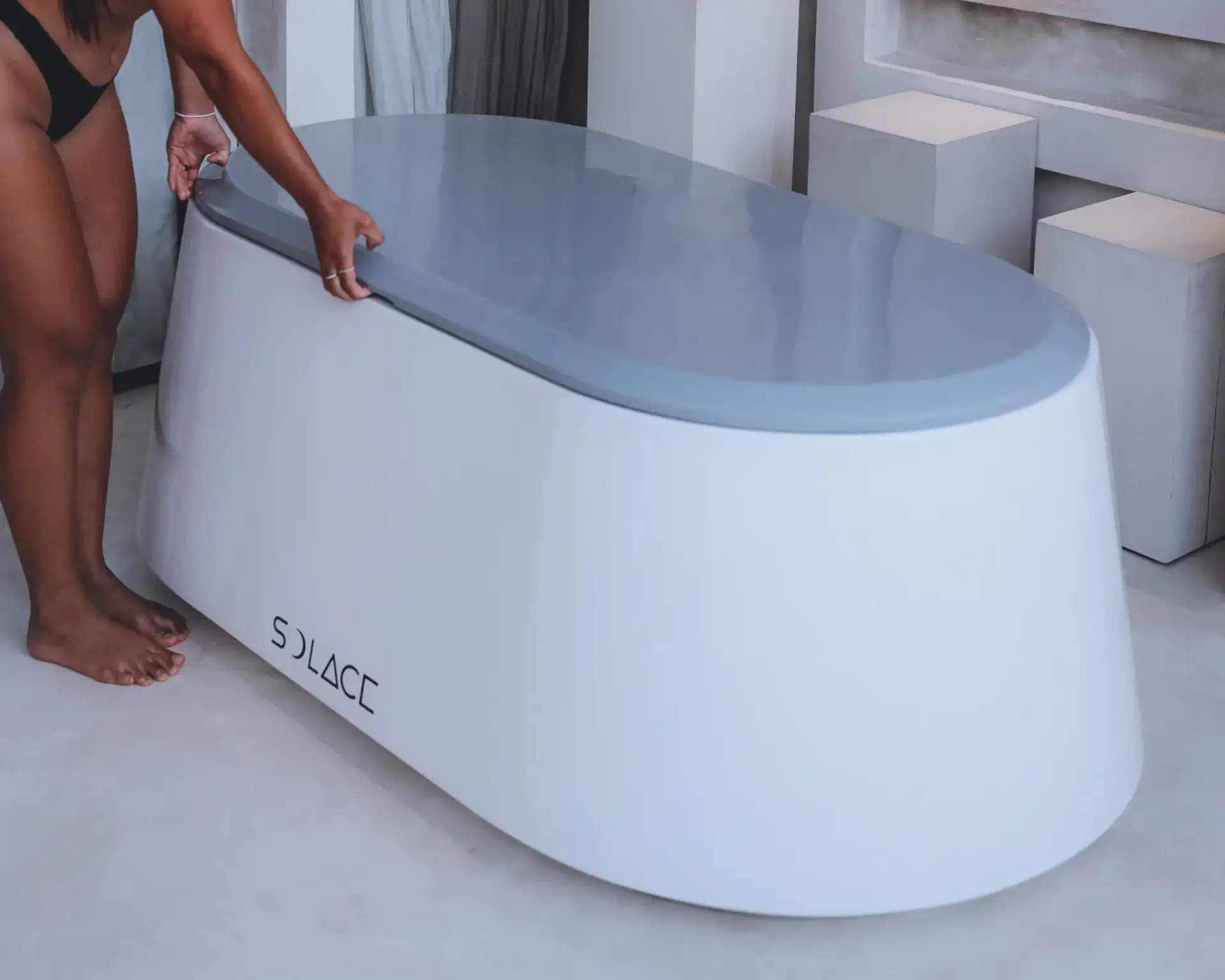 Woman lifting the insulated lid of a Solace residential ice bath before a cold plunge